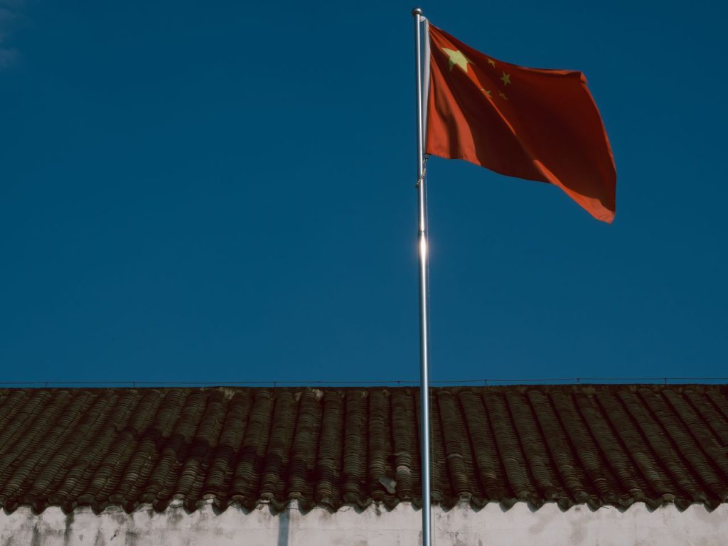 Chinese flag waving over traditional building roof against a clear blue sky. Visiter la Chine pour la première fois